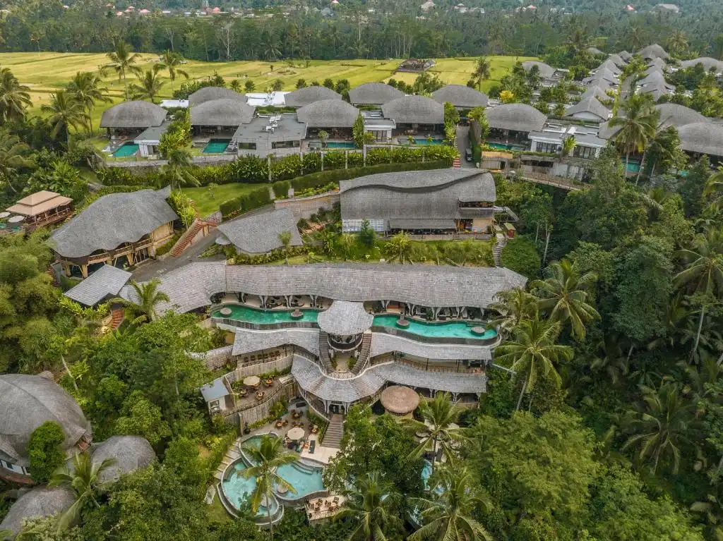 An aerial view of a sprawling hillside property featuring multi-level cascading infinity pools, traditional thatched-roof architecture, and lush jungle surroundings, exemplifying the stunning design of the best luxury resorts in Bali.