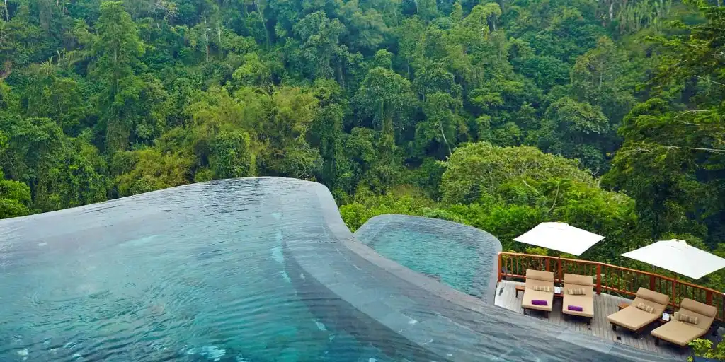 A breathtaking, multi-tiered infinity pool with curved edges overlooking a vast, lush jungle canopy, featuring a wooden lounging deck that captures the incredible views found at the best luxury resorts in Bali.