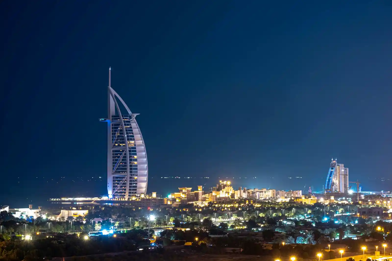 A vibrant nighttime skyline view of the illuminated, sail-shaped Burj Al Arab hotel and surrounding city lights in Dubai, a luxury destination frequently compared to tropical resorts in bali by couples planning their honeymoon.