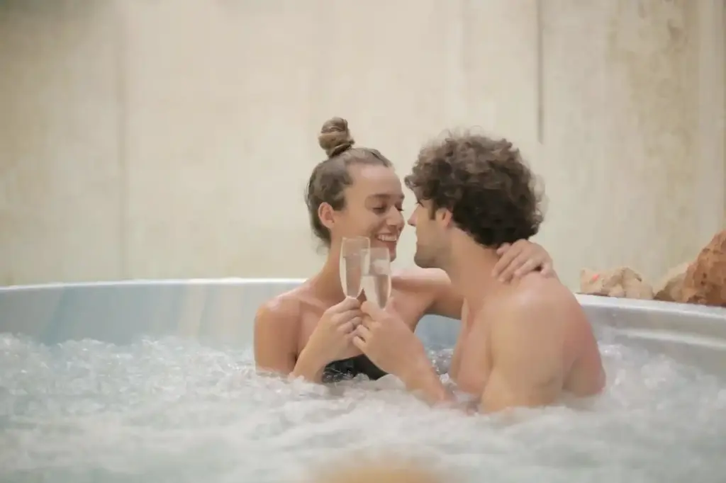 A smiling young couple looks affectionately at each other while toasting with champagne glasses in a bubbling indoor jacuzzi, highlighting the romantic amenities and relaxing experiences offered at resorts in bali.