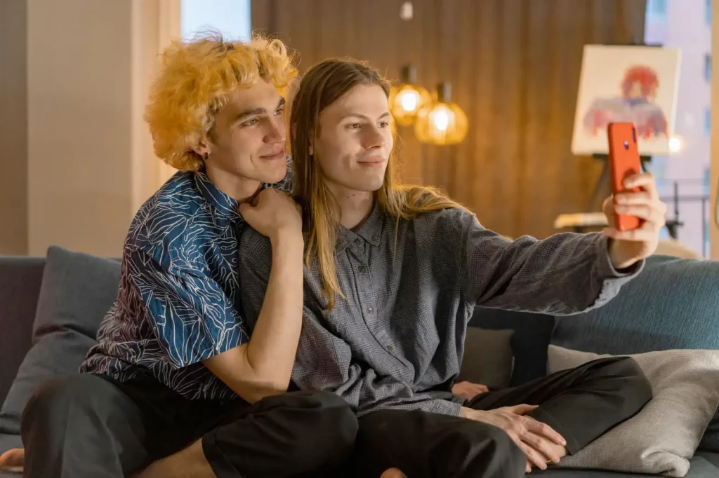 Two men sitting on sofa taking a selfie.