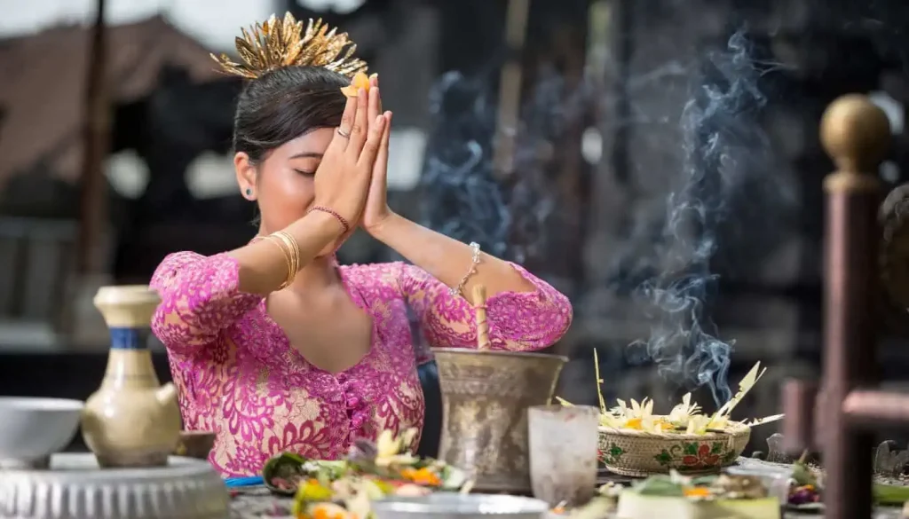 Balinese woman in traditional clothing praying with incense.