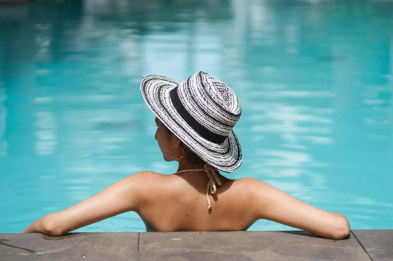 Guest relaxing by turquoise pool at one of the Best luxury Resorts in Indonesia, wearing striped sun hat and swimsuit.