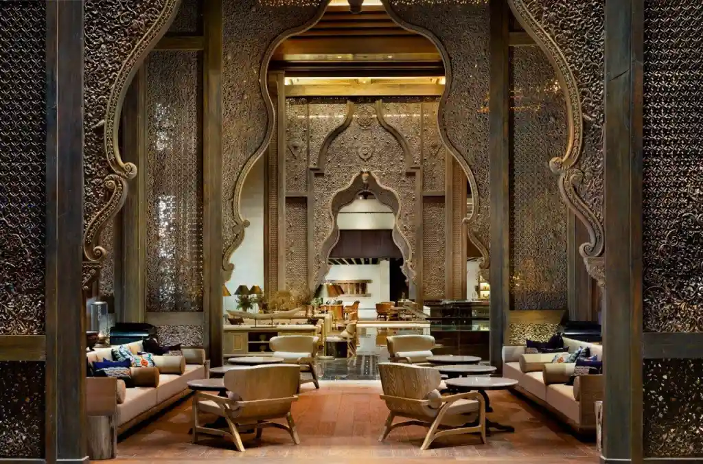 A grand, luxurious lounge framed by magnificent, intricately carved wooden archways, featuring elegant seating areas with warm lighting and deep perspective, showcasing the breathtaking traditional architecture and opulence found in premium resorts in bali.