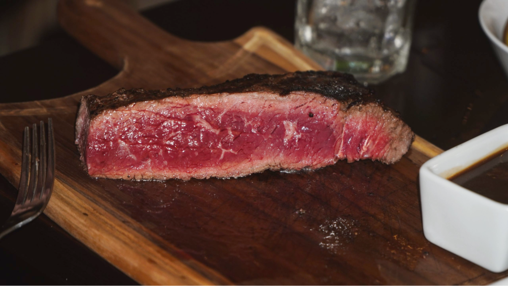 A piece of steak served on a slab of wood with gravy on the side