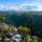 Luxury Bali resort with thatched villas, infinity pools, and tropical forest backdrop under volcanic mountain peaks.