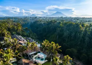 Luxury Bali resort with thatched villas, infinity pools, and tropical forest backdrop under volcanic mountain peaks.
