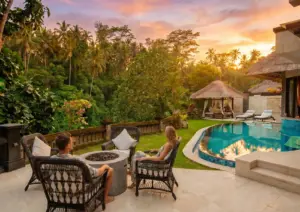 A couple relaxing in wicker chairs around a fire pit beside a private curved pool, enjoying a colorful jungle sunset at a boutique hotel Ubud.