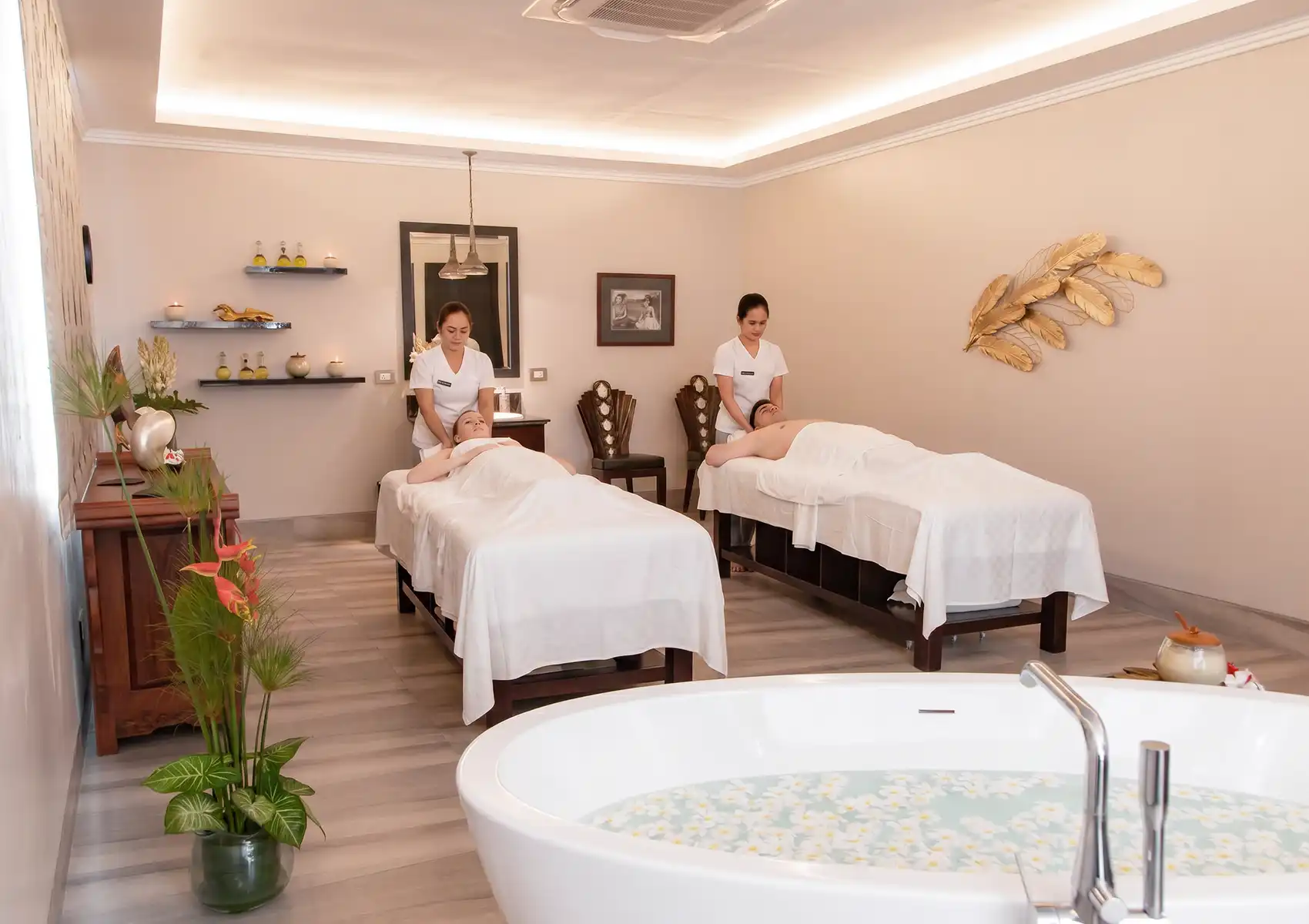 A couple enjoying a relaxing side-by-side massage from two therapists in a luxurious spa room with a large flower petal bath, a perfect rejuvenating activity for a 7 day bali honeymoon.