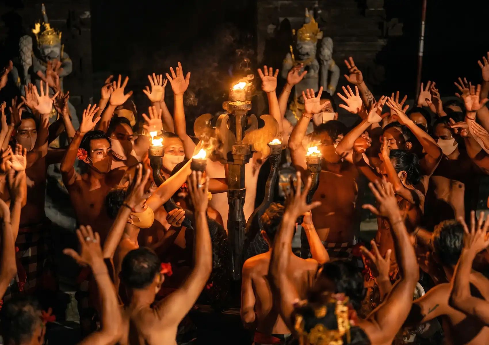 Performers with raised hands surrounding a central fire during a traditional Balinese Kecak dance at night, a captivating cultural experience to include in a 7 day bali honeymoon.