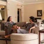 A smiling couple in comfortable grey robes relaxing on a curved sofa in a spacious, luxurious hotel suite, enjoying a quiet morning during their 7 day bali honeymoon.