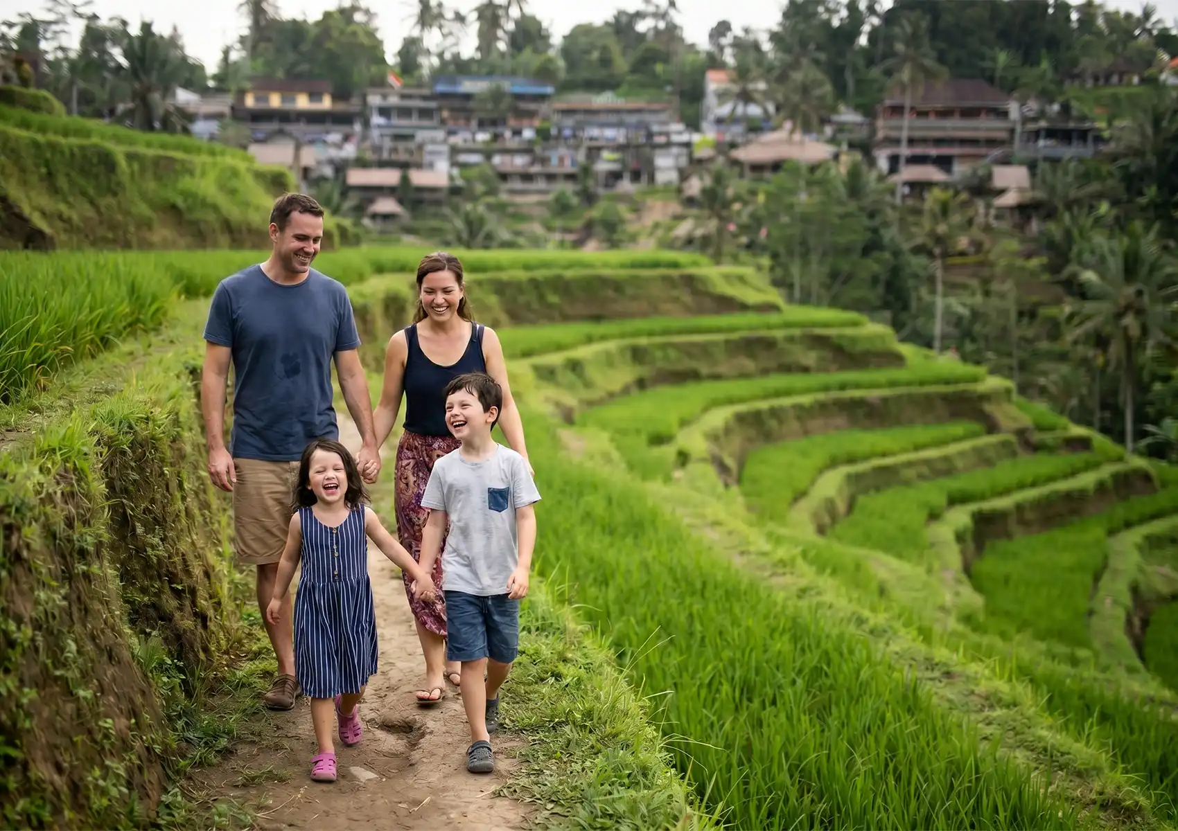 A happy family of four holding hands and laughing as they walk along a scenic dirt path through vibrant green rice terraces, enjoying an adventurous family holiday in Ubud.