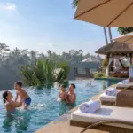 A joyful family of four splashing and playing together in a stunning infinity pool overlooking a lush tropical jungle during a perfect family holiday in Ubud.