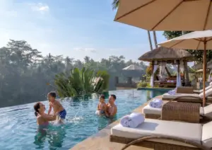 A joyful family of four splashing and playing together in a stunning infinity pool overlooking a lush tropical jungle during a perfect family holiday in Ubud.