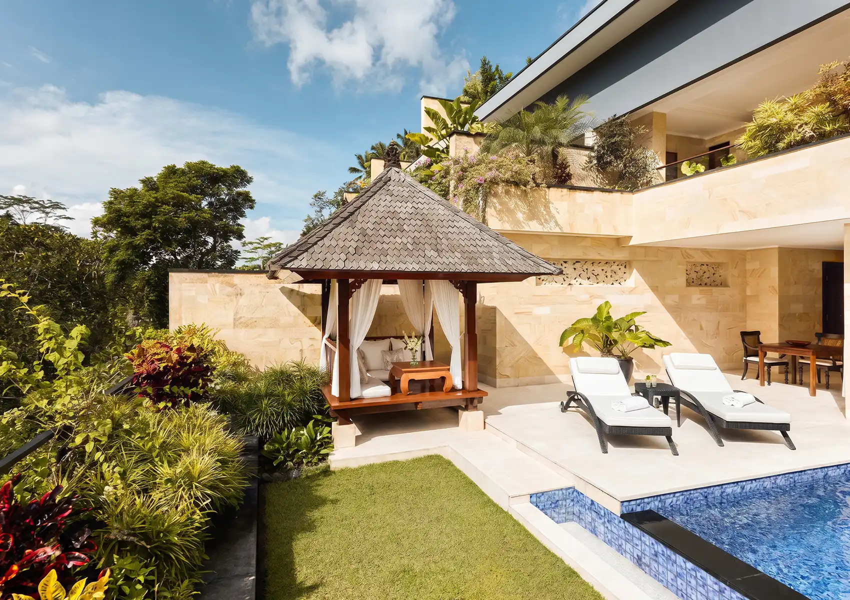 A beautiful luxury villa terrace featuring a private pool, white sun loungers, and a traditional wooden gazebo overlooking a lush green tropical jungle, providing an idyllic stay for a 7 day bali honeymoon.