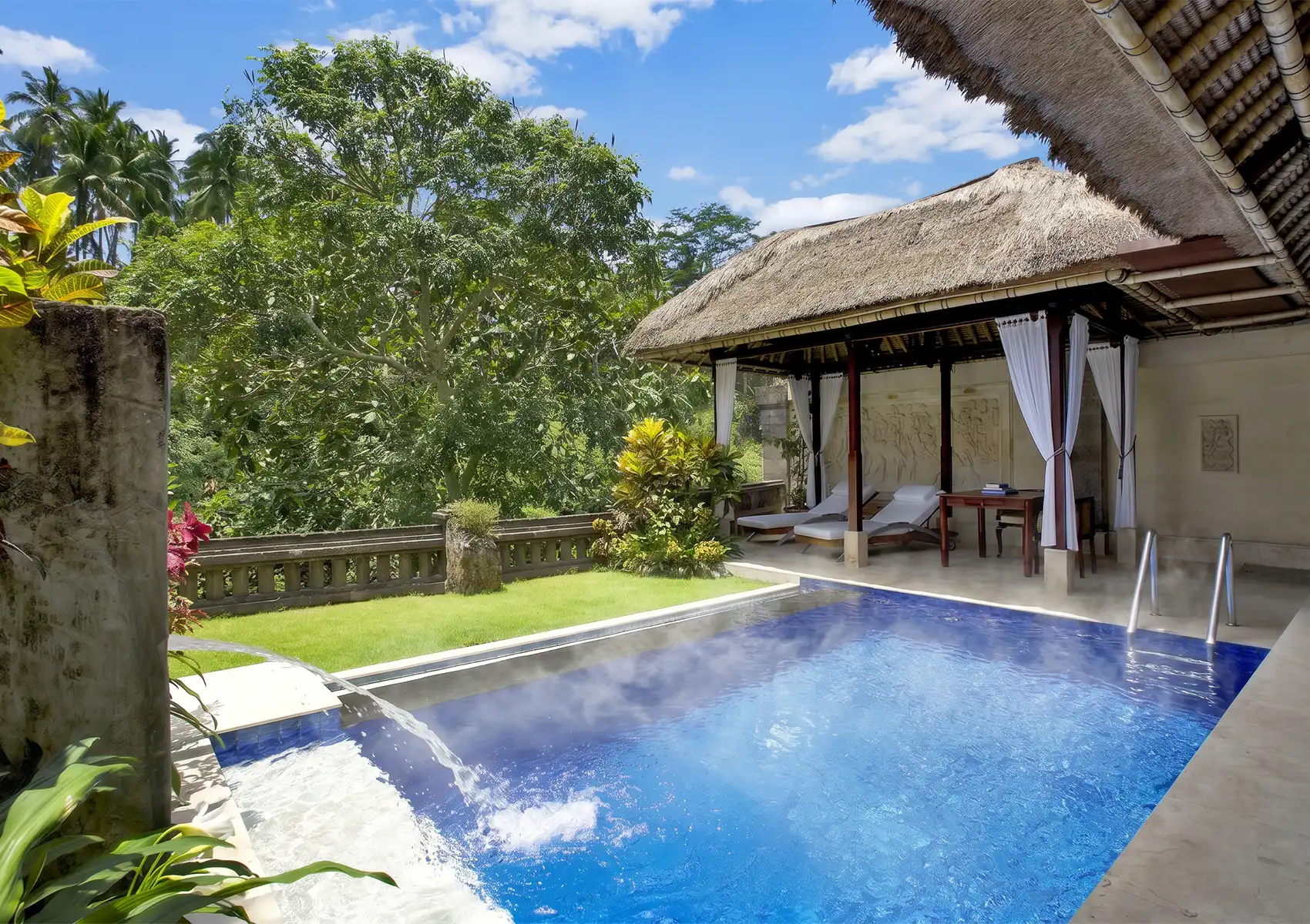 An elegant outdoor living area with dark leather sofas and a wooden coffee table, overlooking a steaming heated swimming pool at a beautiful private pool villa Ubud.