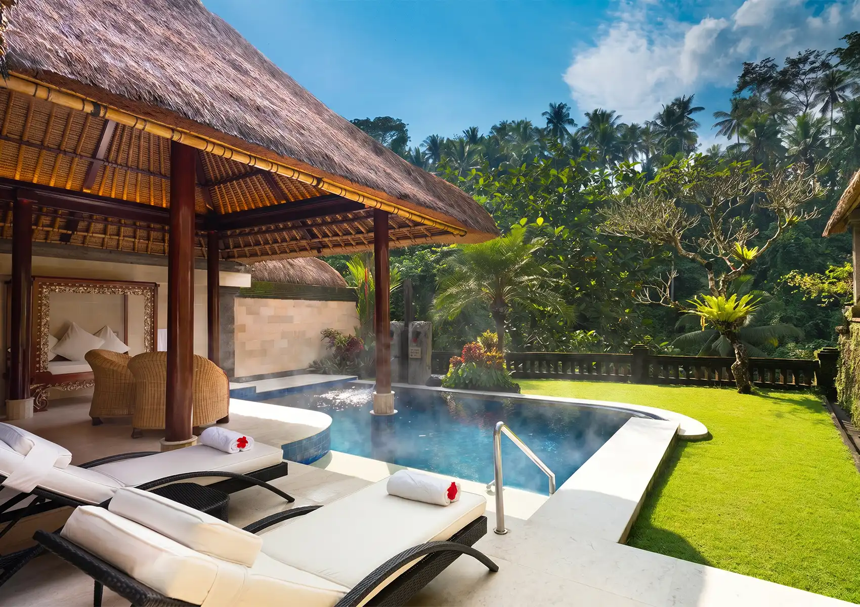 A steaming heated swimming pool beside lounge chairs and a traditional thatched-roof pavilion, showcasing a luxurious Private pool villa ubud surrounded by lush tropical greenery.