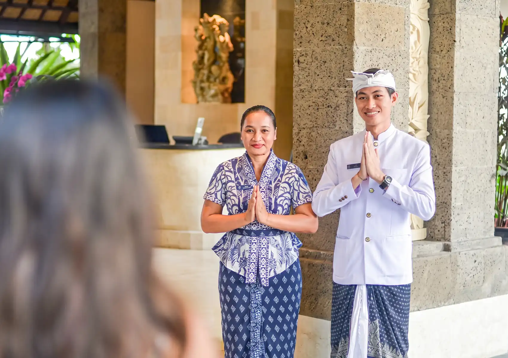 Welcoming hotel staff in traditional Balinese attire greeting a guest with a warm smile, highlighting the authentic hospitality experienced during a bali trip itinerary 10 days.