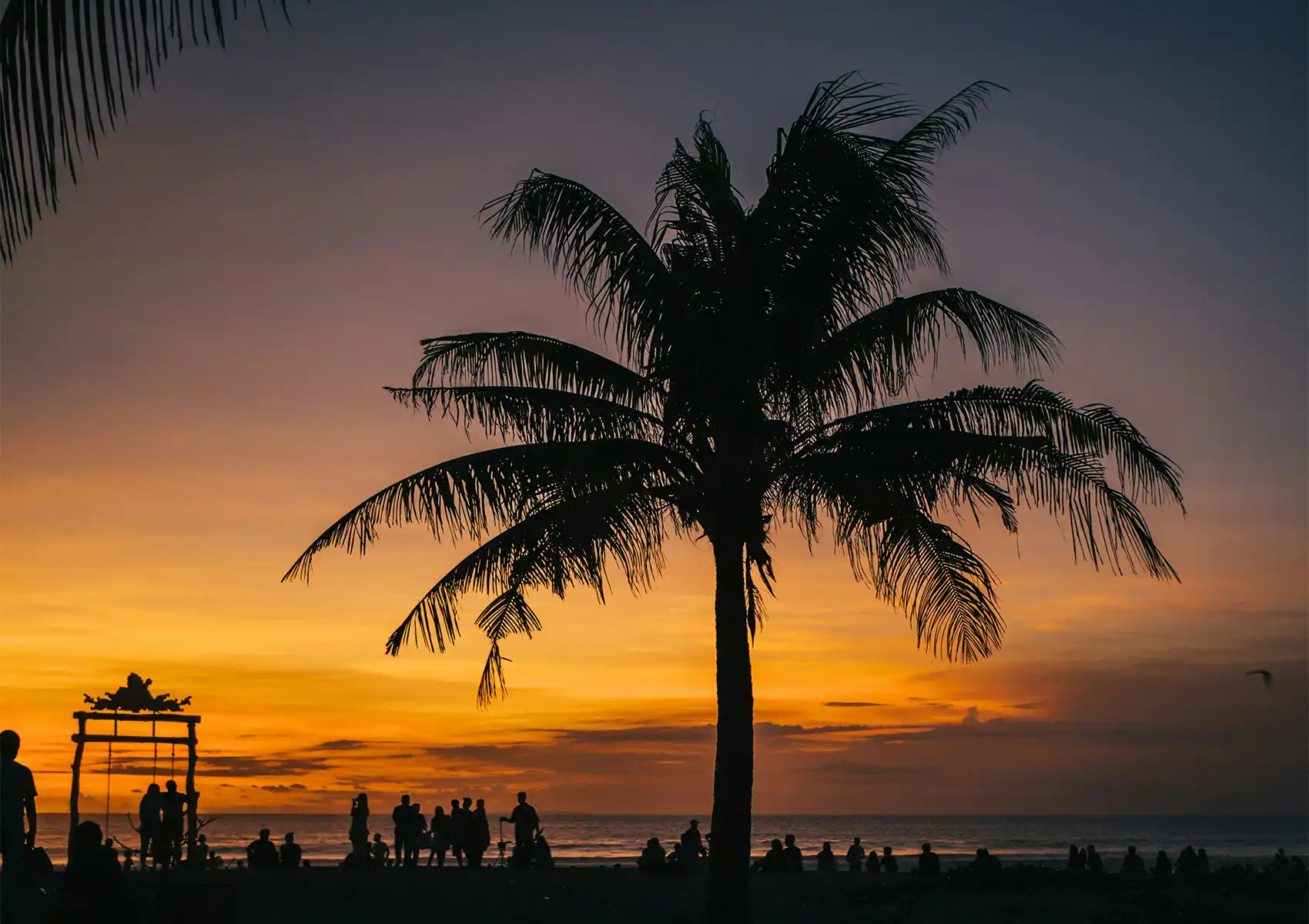 Silhouetted palm trees and travelers enjoying a vibrant golden sunset along the ocean shore, a must-see stop on a bali trip itinerary 10 days.
