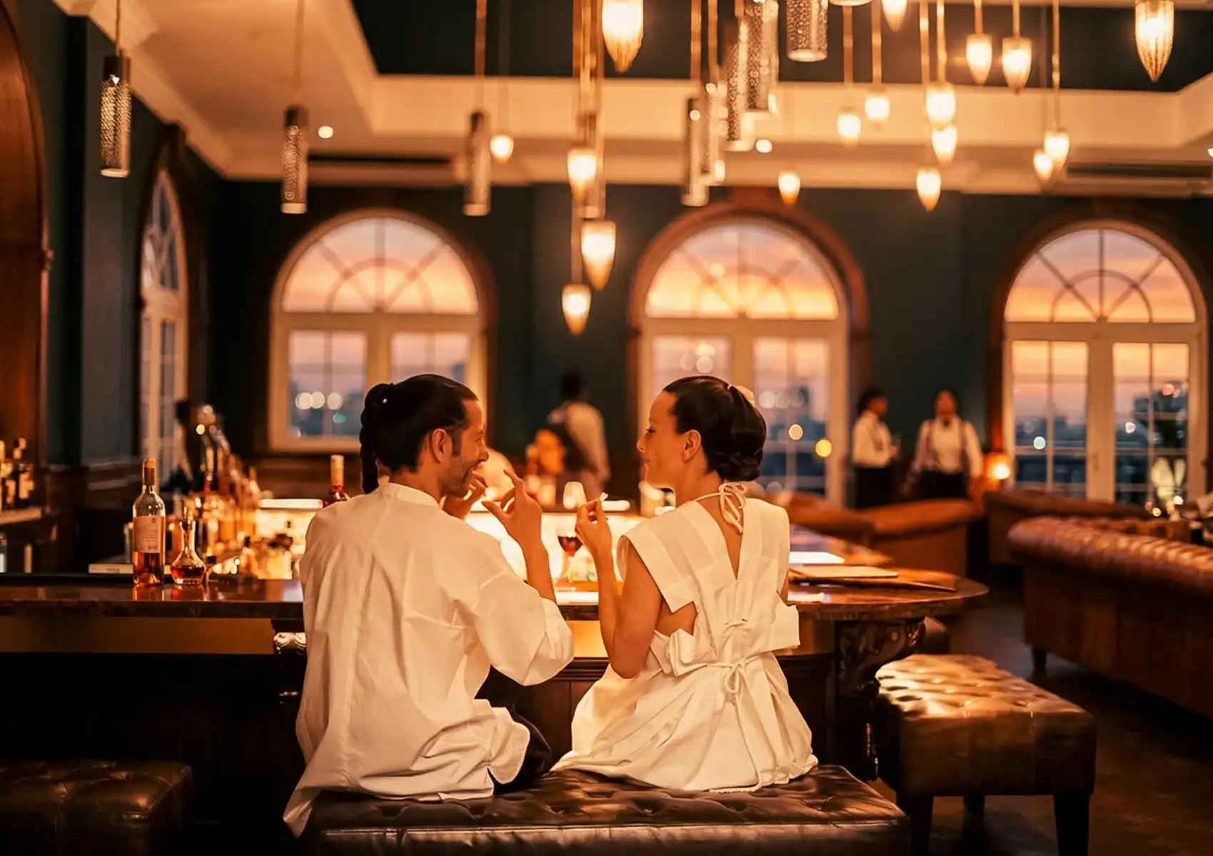 A couple enjoying cocktails at a 1930s-themed speakeasy bar with elegant lighting, arched windows, and sunset views inside a luxury boutique hotel Ubud.