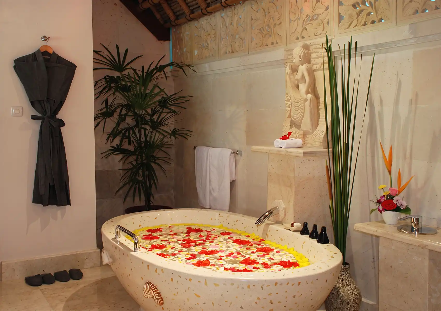 A luxurious stone bathtub filled with fresh flower petals, featuring reusable ceramic amenity bottles that support a zero waste lifestyle.