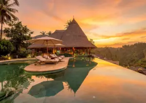 A luxury resort infinity pool reflecting a vibrant golden sunset over tropical jungle hills, highlighting relaxing outdoor things to do in Ubud.