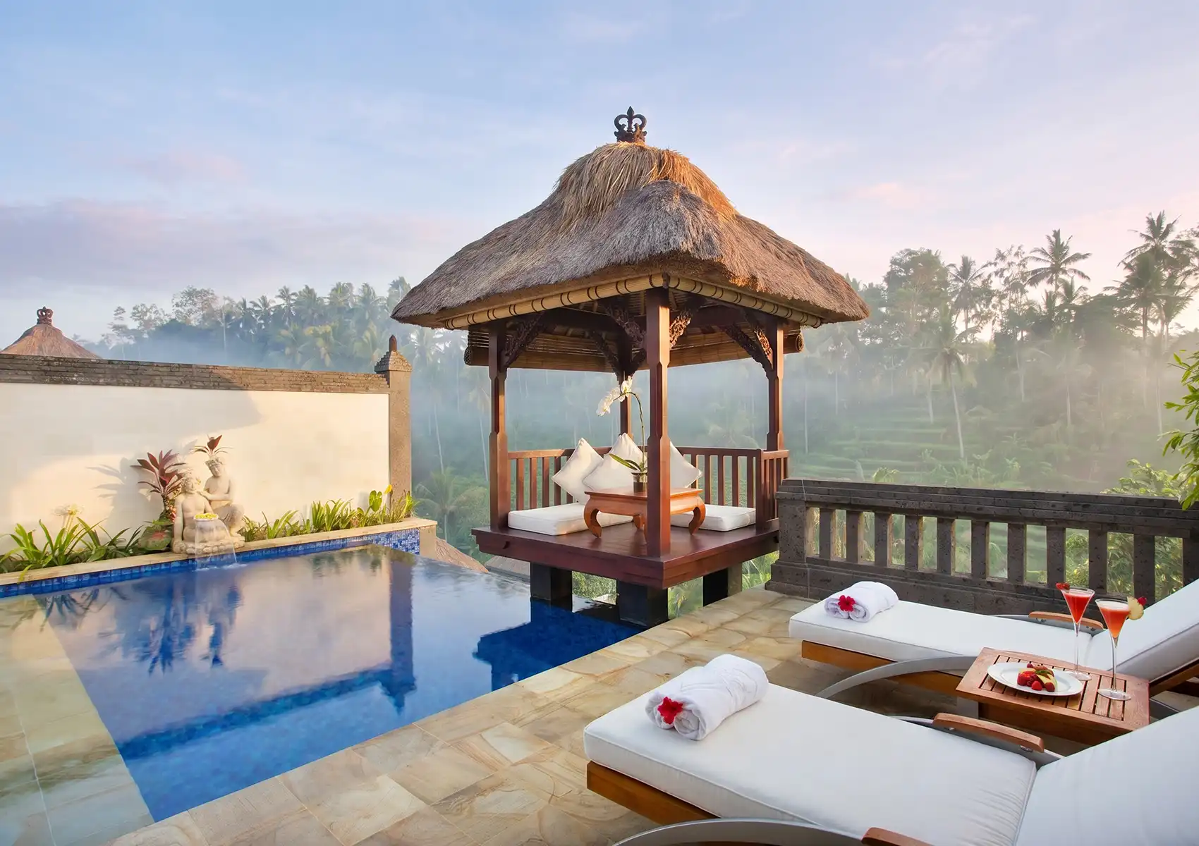 Sun loungers with cocktails beside a private pool and gazebo overlooking misty rice terraces, illustrating luxurious wellness things to do in Ubud.