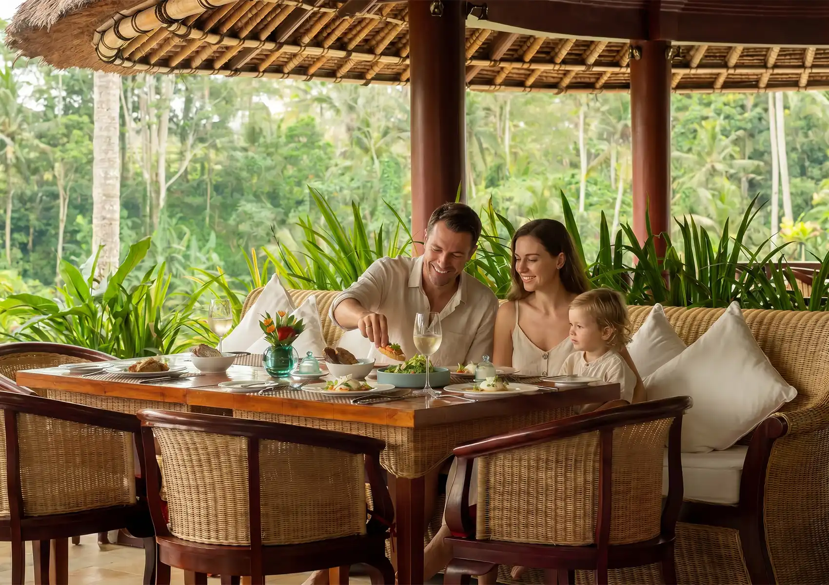 A happy family enjoying a meal together at an open-air tropical restaurant with jungle views, a perfect dining recommendation for your Ubud travel guide.
