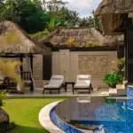 A tranquil outdoor space featuring a curved blue-tiled pool, sun loungers, and intricate Balinese stone wall carvings at a serene boutique hotel Ubud.