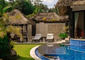A tranquil outdoor space featuring a curved blue-tiled pool, sun loungers, and intricate Balinese stone wall carvings at a serene boutique hotel Ubud.