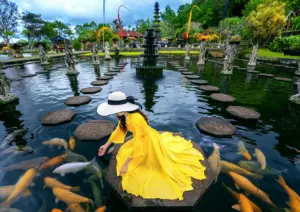 A woman in a vibrant yellow dress feeding large koi fish at a stunning Balinese water temple, showcasing a must-see cultural destination featured in an Ubud travel guide.