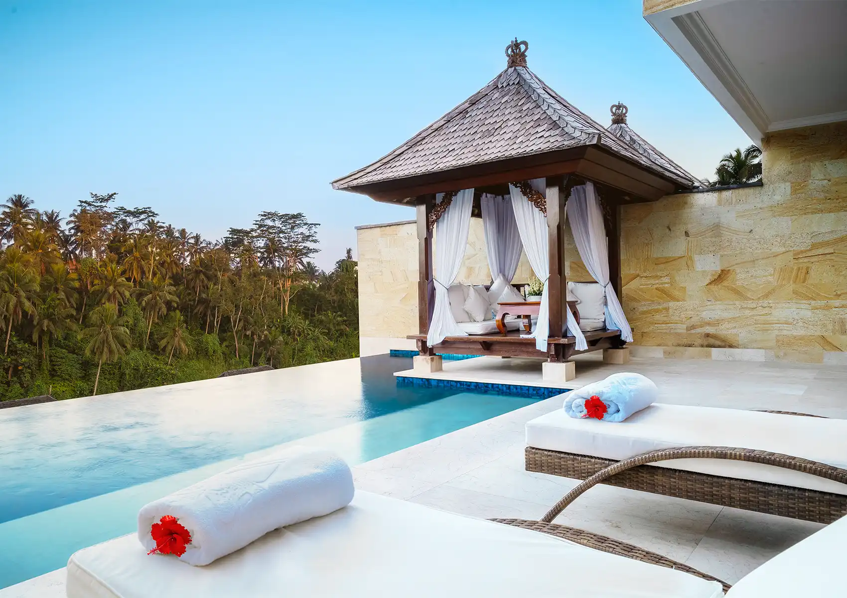 A stunning infinity edge swimming pool overlooking a dense jungle valley, featuring a relaxing traditional gazebo with white curtains at a beautiful Private pool villa ubud.