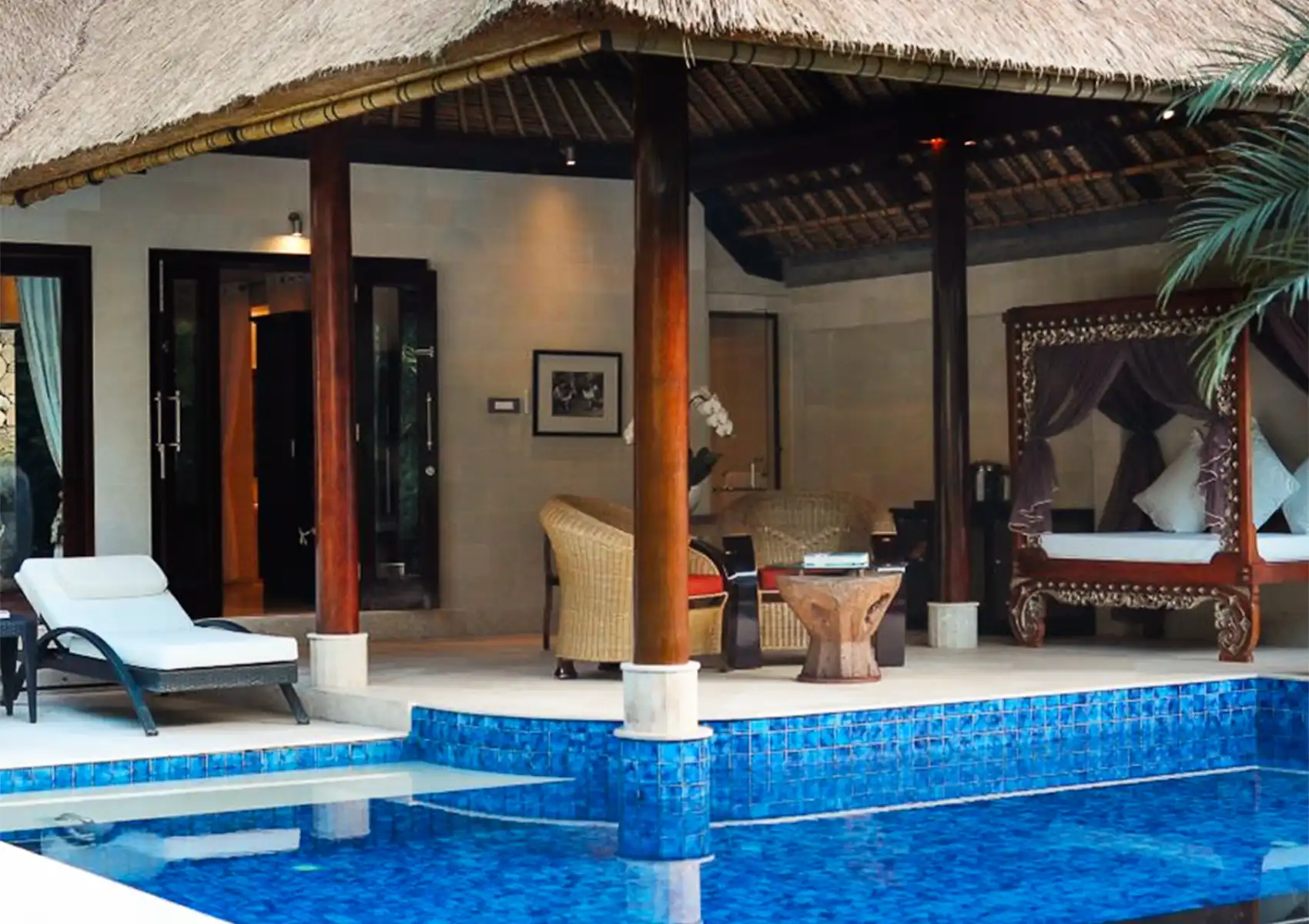 A luxurious private villa featuring a thatched-roof patio, a traditional carved wooden daybed, and a blue-tiled plunge pool at a boutique hotel bali.