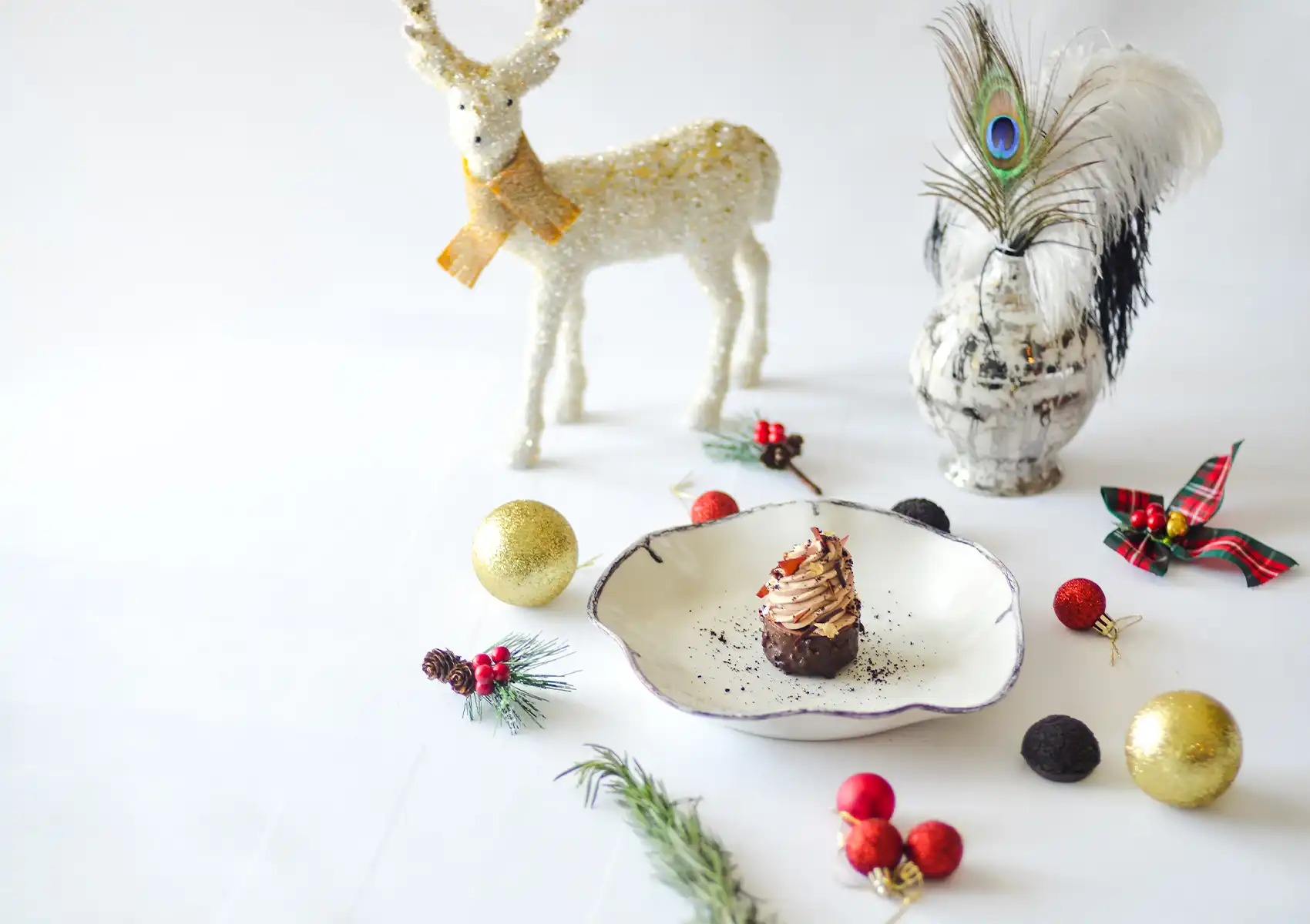 A festive holiday dessert plated on a white table decorated with Christmas baubles, pine branches, and a glittering white reindeer at a boutique hotel in Ubud.