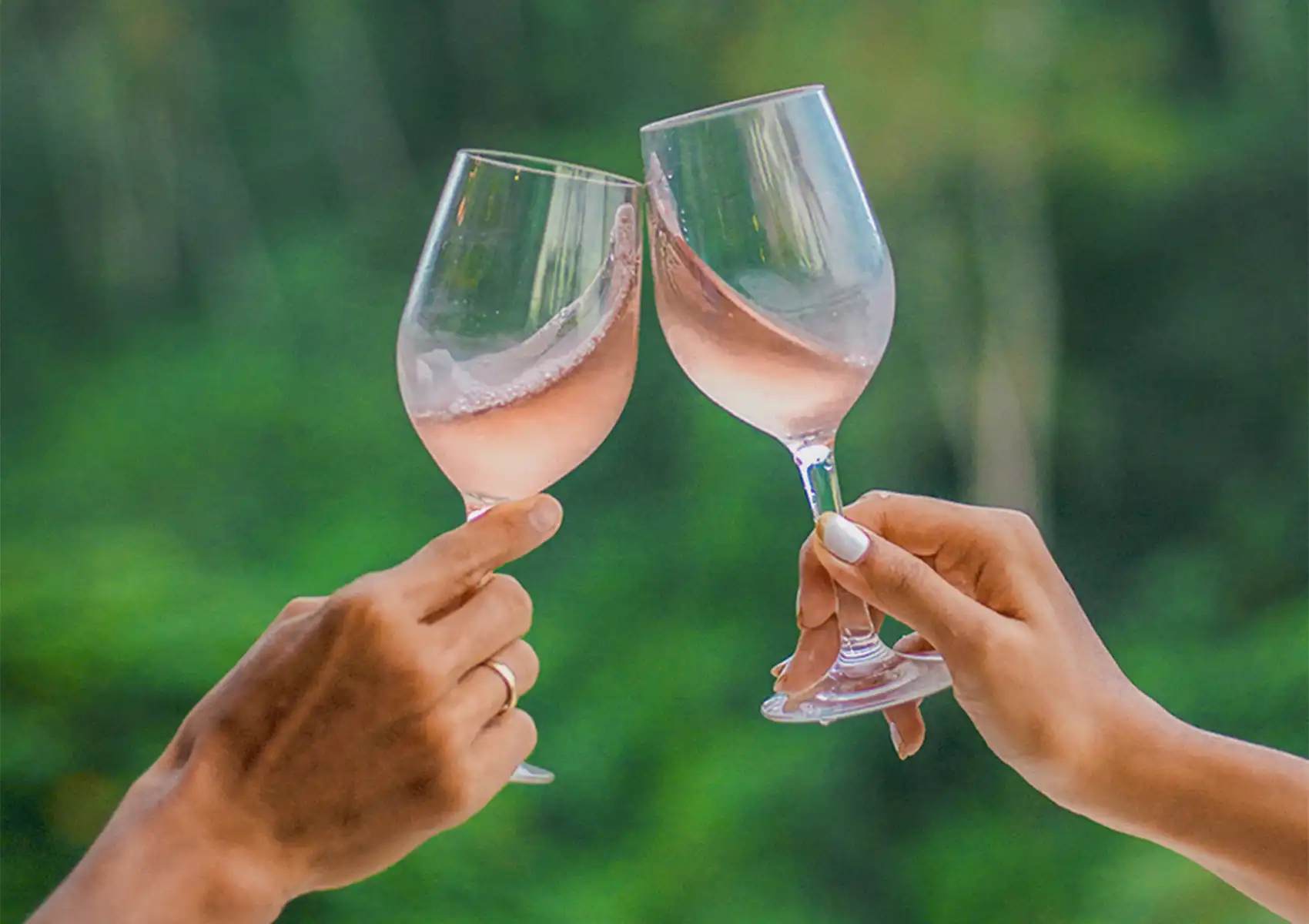 Two people holding wine glasses clinking them in a toast with a blurred green background at a boutique hotel bali.