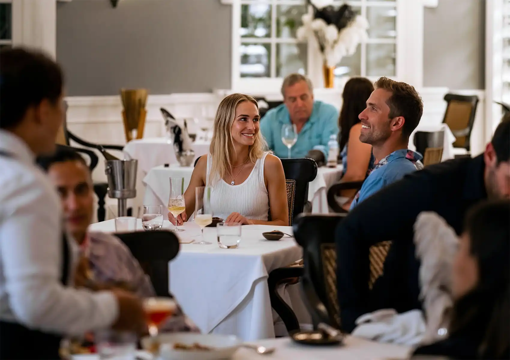 A smiling couple enjoying a dining experience at a white-clothed table in an elegant restaurant setting at a boutique hotel bali.