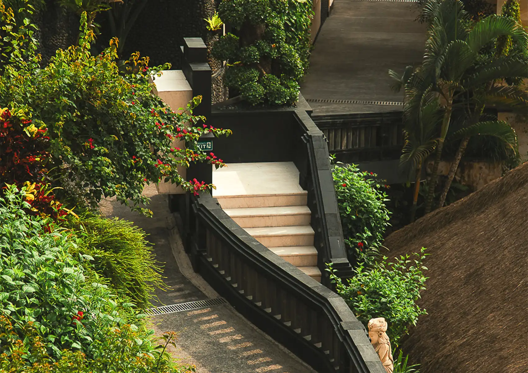 A stone stairway with dark railings descending through a lush, landscaped garden with vibrant flowers and tropical foliage at a boutique retreat in bali.