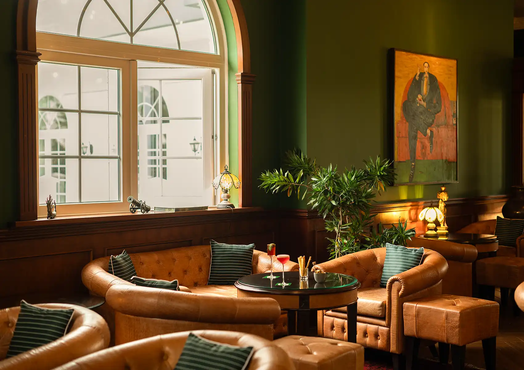 Elegant lounge area featuring green walls, tufted leather sofas, and an arched window inside a private pool villa Ubud.