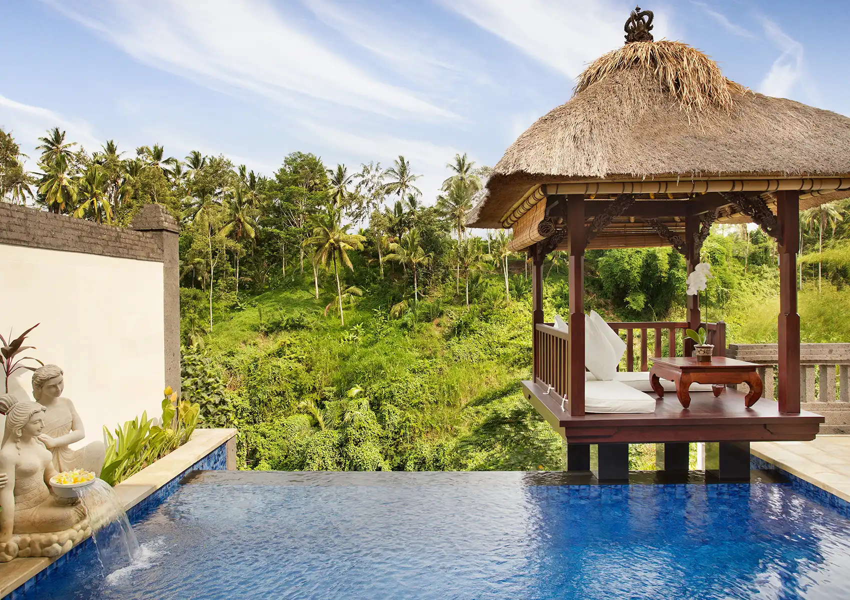 A private infinity pool with stone fountain statues and a traditional thatched-roof pavilion overlooking a tropical jungle valley at a boutique hotel Bali.