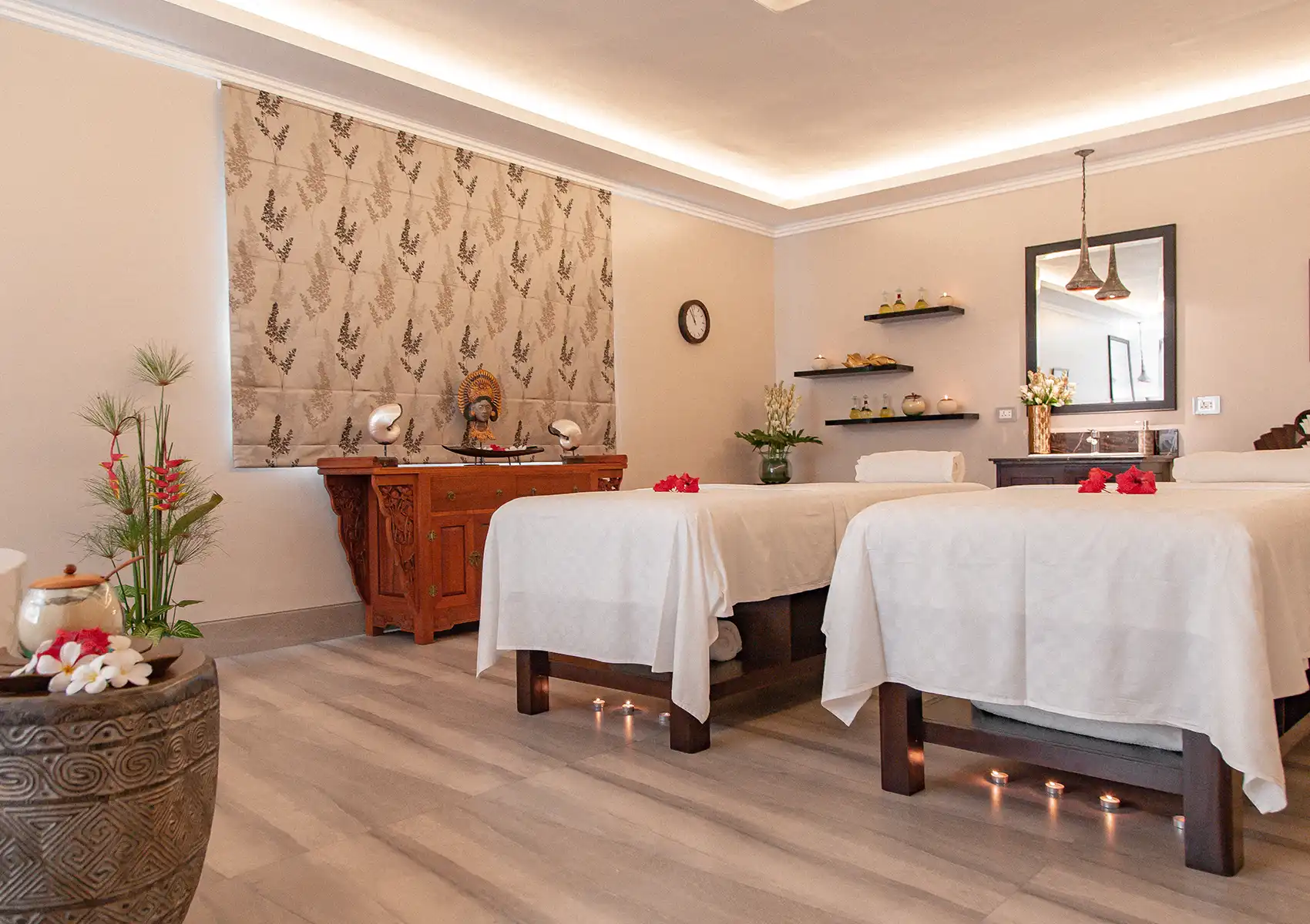A tranquil couples treatment room featuring two massage beds adorned with red flowers, traditional Balinese decor, and ambient floor candles at a boutique retreat in bali.