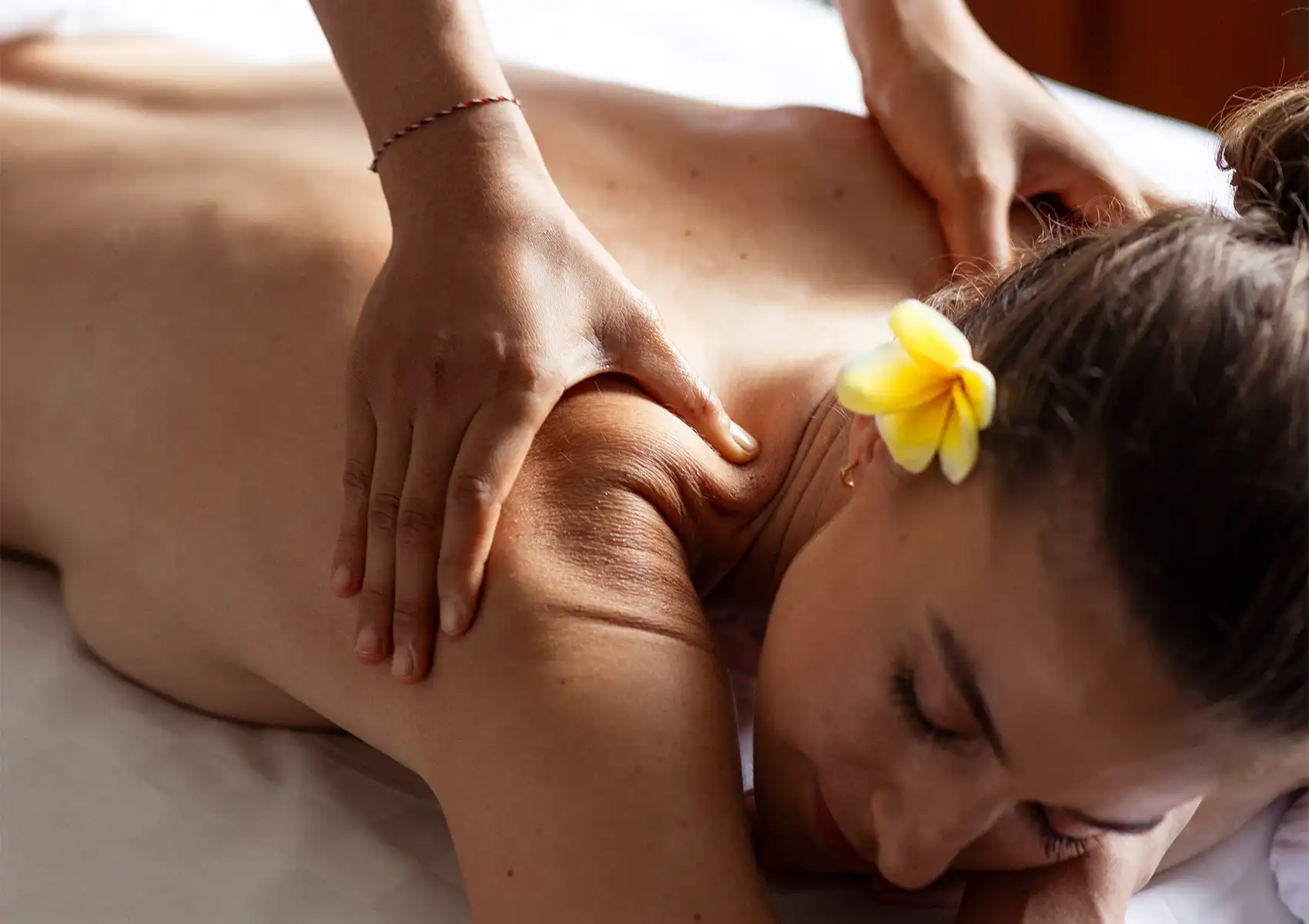 A woman with a yellow frangipani flower in her hair receiving a relaxing back and shoulder massage at a spa in a boutique hotel Bali.
