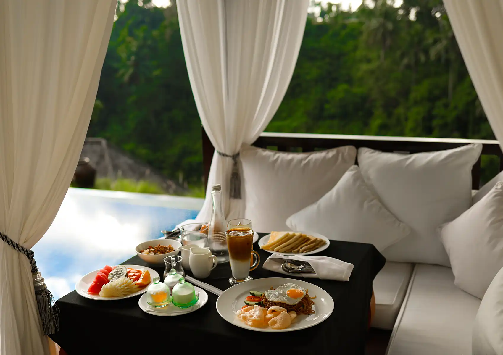 A luxurious breakfast spread served on a draped cabana daybed overlooking the lush jungle at a private pool villa Ubud.